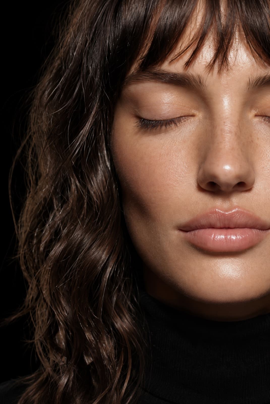 Primo piano di donna con pelle luminosa e occhi chiusi su fondo scuro