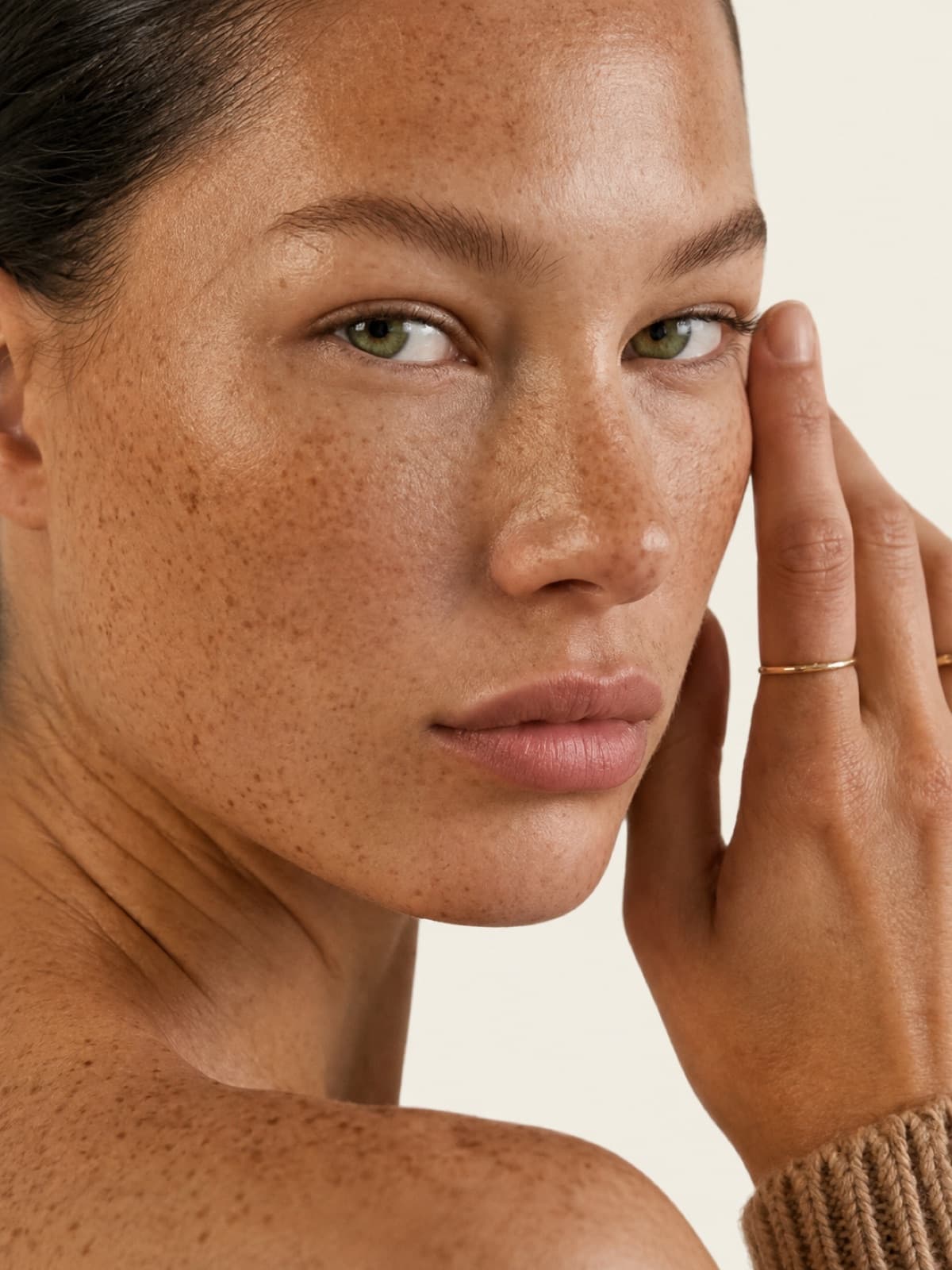 Viso di donna con pelle luminosa e uniforme, mano al viso, luce naturale